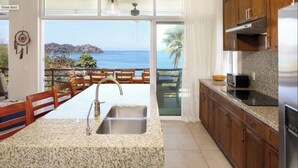 A kitchen with granite countertops, stainless steel appliances, and a view of the ocean.