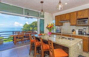 A kitchen with granite countertops, wooden cabinets, and a view of the ocean. - Vista al Mar - Monterosa (Sayulita)