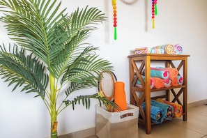 A room with a potted plant, a shelf with folded towels, and a tennis racket.