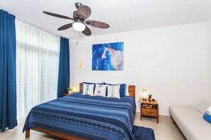 A bedroom with a bed, a nightstand, a lamp, a ceiling fan, and a painting on the wall. - Vista al Mar - Monterosa (Sayulita)