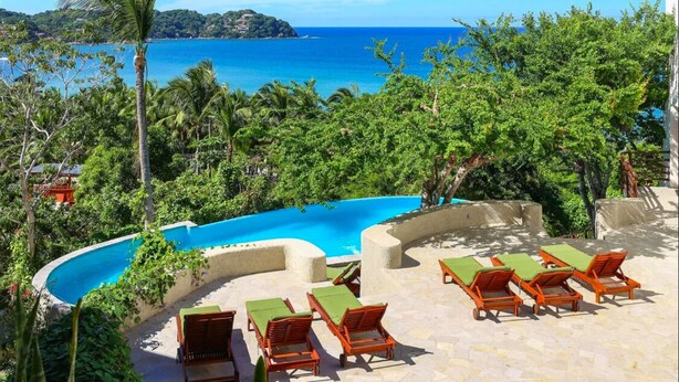 A pool area with lounge chairs and a view of the ocean.