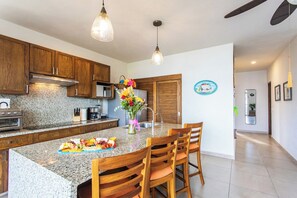A kitchen with granite countertops, wooden cabinets, a central island with chairs, and pendant lighting.
