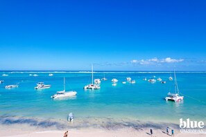 A beach with several boats anchored in the water and people walking on the shore.