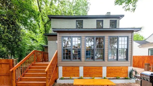Une maison à deux étages avec un escalier en bois, une terrasse dotée d’une table de pique-nique et d’un barbecue.