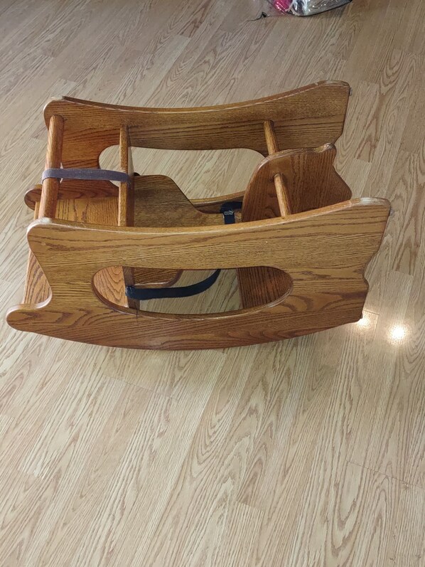 Una mecedora de madera con respaldo y reposabrazos curvos, sobre un piso de madera.