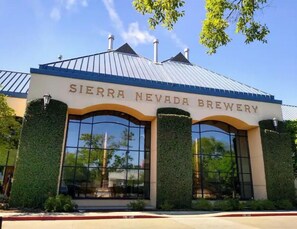 Exterior de la Sierra Nevada Brewery, con techo metálico, amplias ventanas y follaje verde a los lados.
