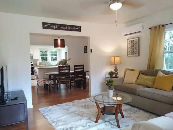 A living room with a sofa, a glass coffee table, and a dining area with chairs and a table.