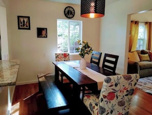 Uma sala de jantar com mesa de madeira, cadeiras, um vaso com flores e um relógio de parede.
