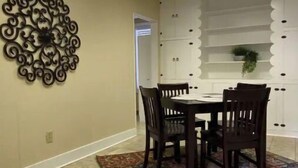 A dining area with a round table, four chairs, a decorative wall piece, and a patterned rug. - The Downtown Den (Pikeville)