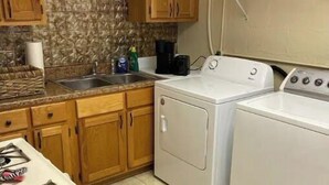 A kitchen with wooden cabinets, a gas stove, a washing machine, and a coffee maker. - The Downtown Den (Pikeville)