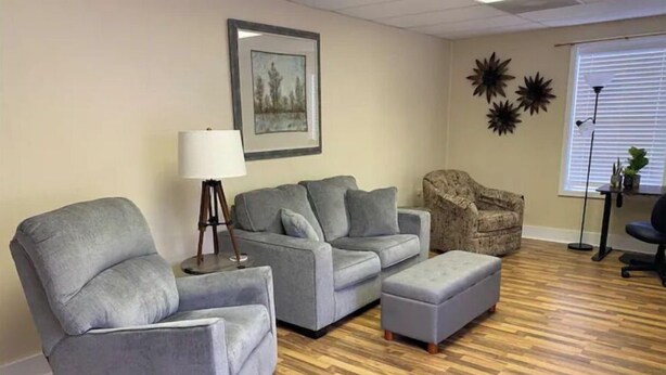 A living room with a grey sofa set, a wooden floor, and a framed picture on the wall. - The Downtown Den (Pikeville)