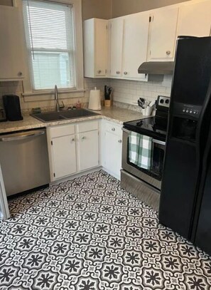 A kitchen with white cabinets, a black refrigerator, and patterned floor tiles.