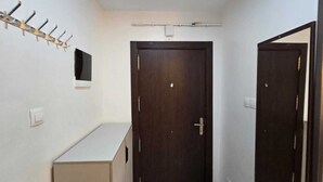 Un couloir étroit avec une porte en bois, un porte-manteau et une petite étagère.