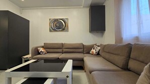 Un salon moderne avec un canapé d’angle, une table basse, un téléviseur à écran plat et un tableau accroché au mur.