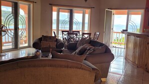 A spacious living area with a sofa, a glass coffee table, and a view of a balcony with outdoor furniture.