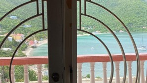 A balcony with white balustrades overlooking a coastal area with a view of the sea and hills.