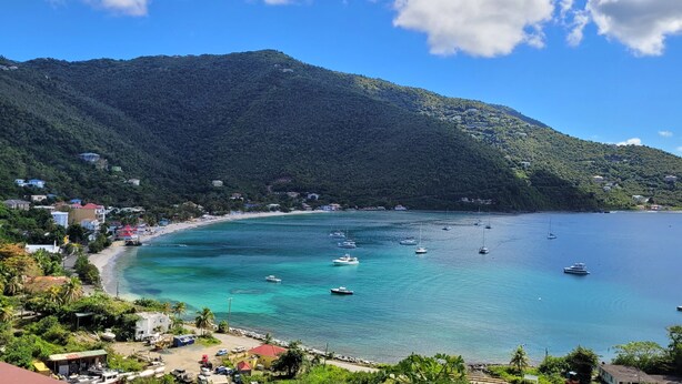 A coastal town with a beach, boats, and a mountainous backdrop.
