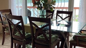 A dining area with a glass table and chairs, a vase with flowers, and a view of a lake and mountains through large windows.