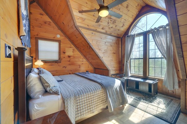 Cozy cabin with a sloped ceiling, featuring a bed, window, and arched window offering a view of the outdoors.