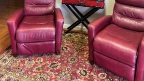 Two red leather armchairs, a small table with a plant, and a framed picture on a plain wall. - The   Nook (Pikeville)