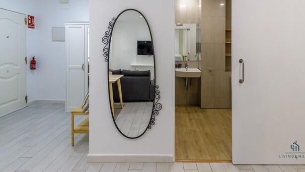 A hotel room with a large mirror, a sofa, a small table, and a bathroom with a sink and mirror.