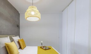 A bedroom with a bed, pillows, a bedside table with a tray, and a hanging light fixture.
