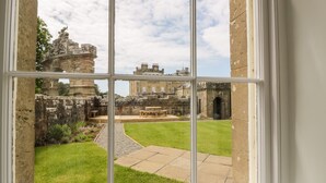 A view through a window of a courtyard with stone walls, a grassy area, and a bench. - Clocktower - Culzean Castle (Maybole)