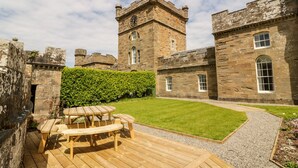 A courtyard with a wooden deck and picnic table, surrounded by stone buildings with a clock tower. - Clocktower - Culzean Castle (Maybole)
