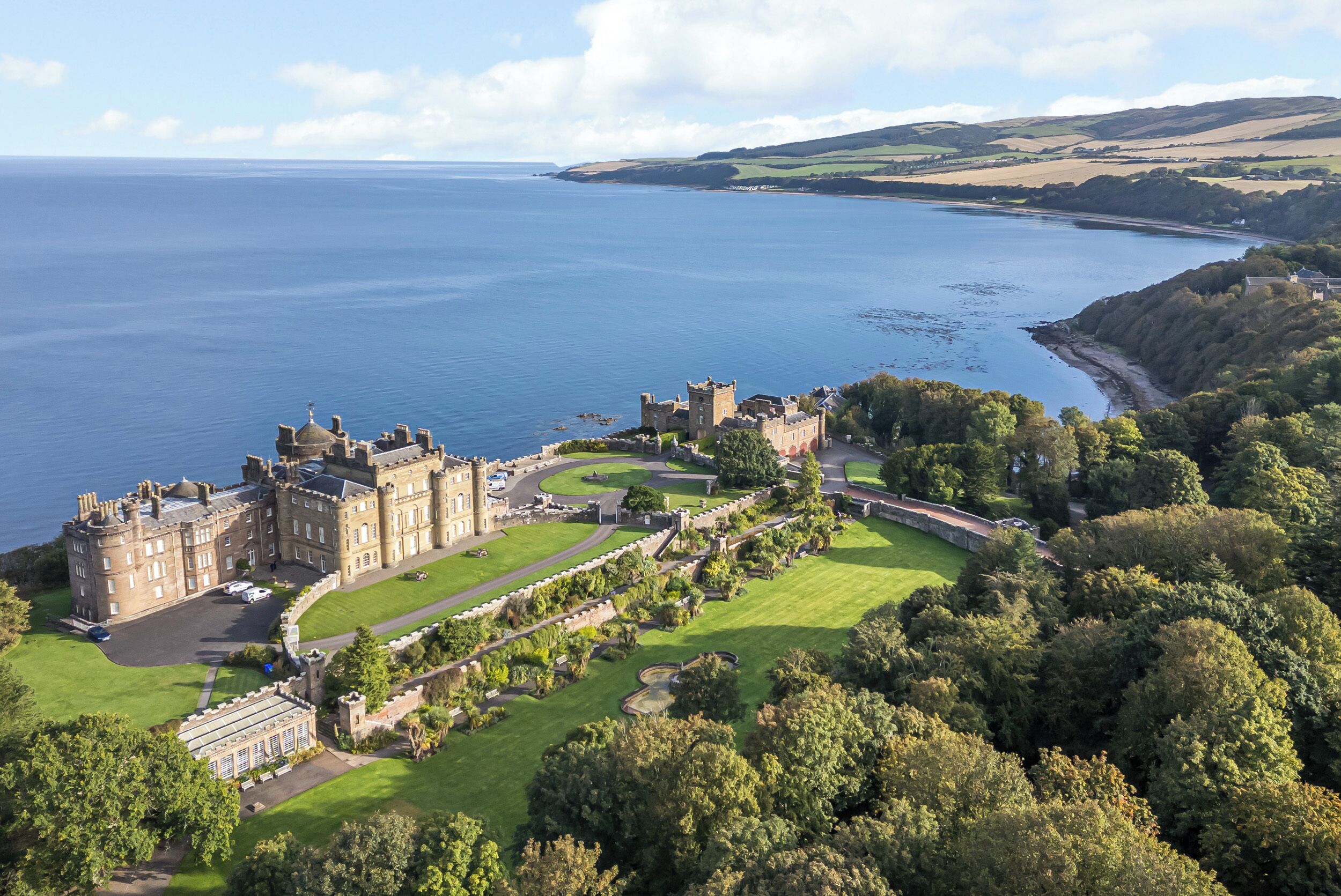 A castle with a large lawn, a driveway, and a view of the sea.