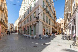 Una calle con mesas al aire libre, edificios con balcones y un cielo despejado.