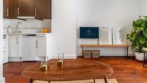 Une cuisine moderne avec des meubles en bois, un plan de travail blanc et un coin repas doté d’une table ronde. Des œuvres d’art encadrées ornent le mur, et une plante en pot se trouve dans un coin.