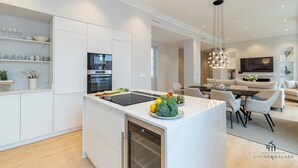Een moderne keuken met witte kasten, een inbouwoven en een eethoek met een tafel en stoelen.