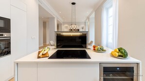 Een moderne keuken met een inbouwoven, een centraal kookeiland met een zwart inductiekookplaatje en een hangende lamp.