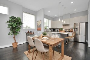 A modern kitchen with dark wood flooring, white cabinets, stainless steel appliances, and a dining area with a wooden table and chairs.