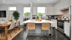 Uma cozinha moderna com armários brancos, eletrodomésticos de aço inoxidável e uma ilha central com banquetas.