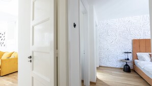 A modern bedroom with a wooden floor, a bed with white bedding, a yellow sofa, and a patterned wall.