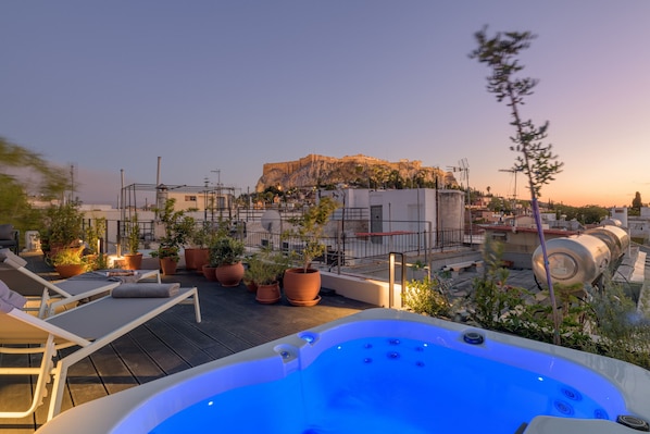 Relax on the rooftop terrace with a hot tub and lounge chairs, taking in the view of a historic building and a striking rock formation.
