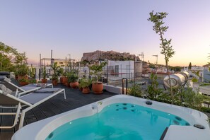 Relax on the rooftop terrace with a hot tub, lounge chairs, and lush potted plants overlooking a historic landmark.