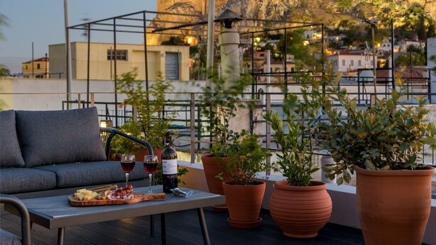 A rooftop terrace with a sofa, table, wine glasses, and a view of a historic hilltop fortress.