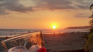 A hand holding a glass with a sunset in the background. - Cozy Iguana Apartmentos 3 (Esterillos Oeste)