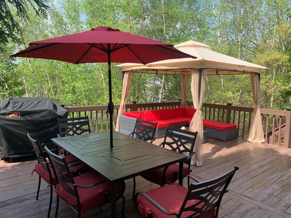 Un área de estar al aire libre techada con mesa y sillas, una parrilla y un pabellón.