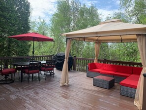 Una terraza techada al aire libre con mesa y sillas, un sofá rojo y una marquesina.