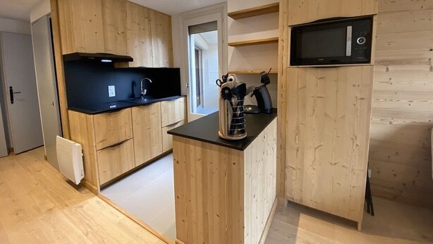 A modern kitchen with wooden cabinetry, a black countertop, and a built-in microwave. - Veronica n°53: T2 with mountain corner (Châtel)