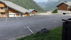 A parking lot with wooden buildings, a wooden bridge, and a mountainous backdrop. - Veronica n°53: T2 with mountain corner (Châtel)