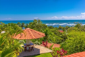 Une terrasse avec une table et des chaises, un toit recouvert de tuiles rouges et une vue sur l’océan.