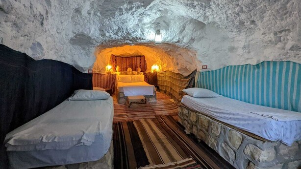 Ein gemütlicher, höhlenähnlicher Raum mit zwei Betten, einer Sitzgruppe mit Tisch und Stühlen sowie einer warmen Lichtquelle.