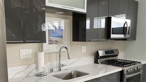 A modern kitchen with dark cabinets, a stainless steel sink, a microwave, and a gas stove. - HB Hideaway · 2 Mi to Beach · 60+ Day Savings · Ideal for Snowbirds & WFH! (Huntington Beach)