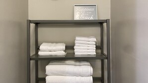 A bathroom with a toilet, a shelf with folded towels, and two wall-mounted sconces. - HB Hideaway · 2 Mi to Beach · 60+ Day Savings · Ideal for Snowbirds & WFH! (Huntington Beach)