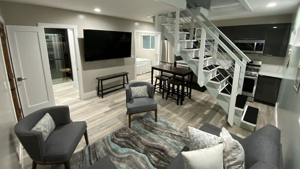 A modern living room with a staircase, a flat-screen TV, and a dining area. - HB Hideaway · 2 Mi to Beach · 60+ Day Savings · Ideal for Snowbirds & WFH! (Huntington Beach)