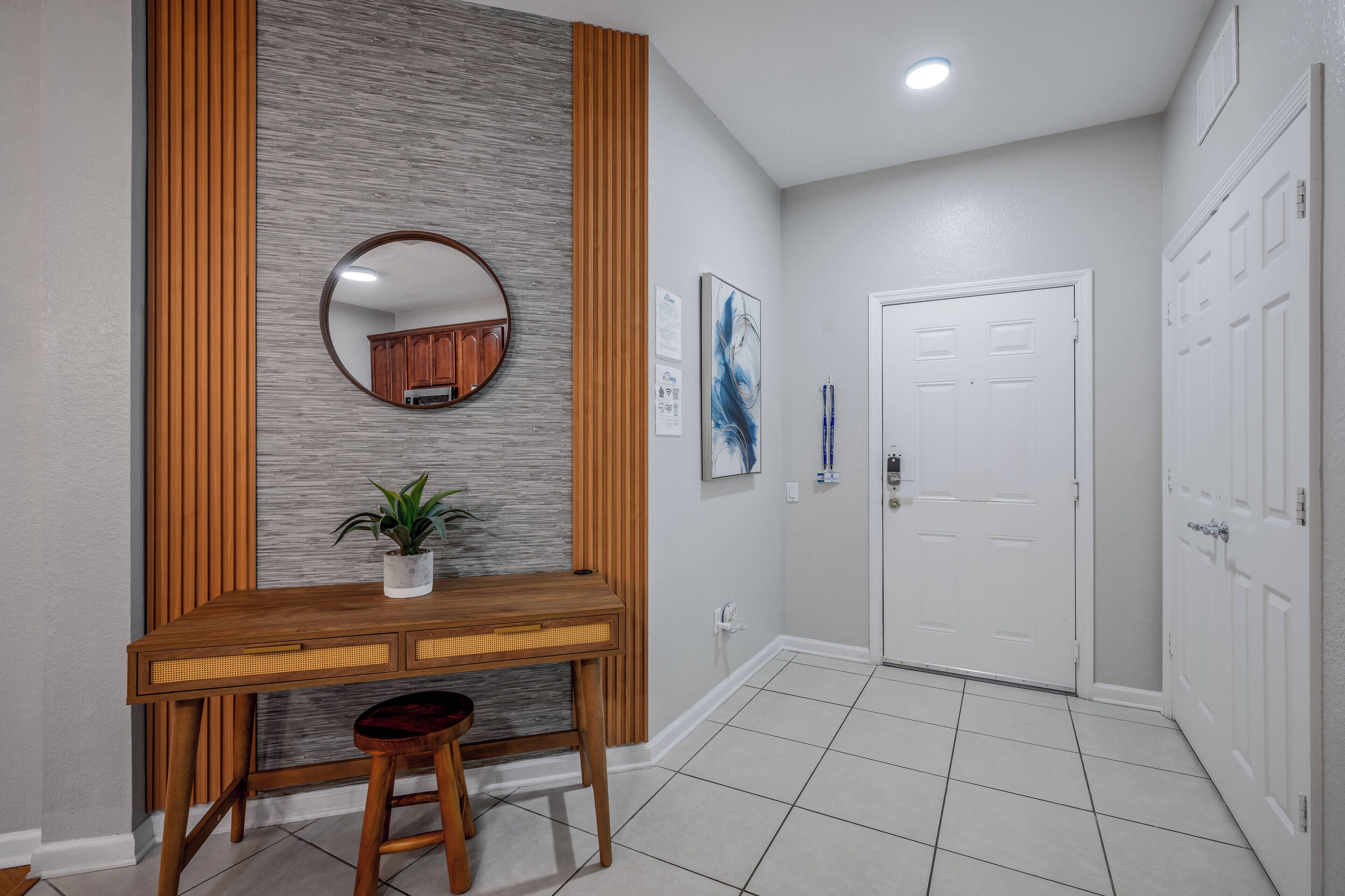 Un couloir avec une console en bois, une plante en pot, un miroir rond et une porte blanche.